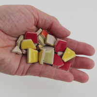 Video of Flip ceramic puzzle pieces in red mix, opaque glazed porcelain, 4–20 mm, held in a hand and poured out to show their shapes and finish