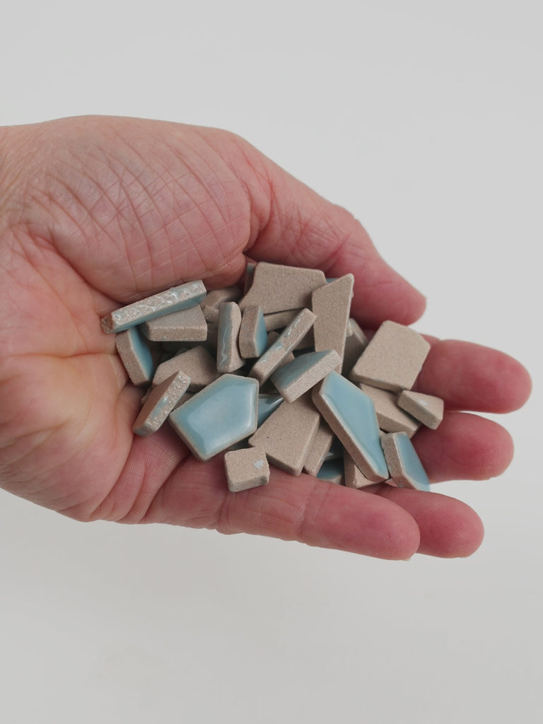Video of Flip ceramic puzzle pieces in ice blue, opaque glazed porcelain, 4–20 mm, held in a hand and poured out to show their shapes and finish