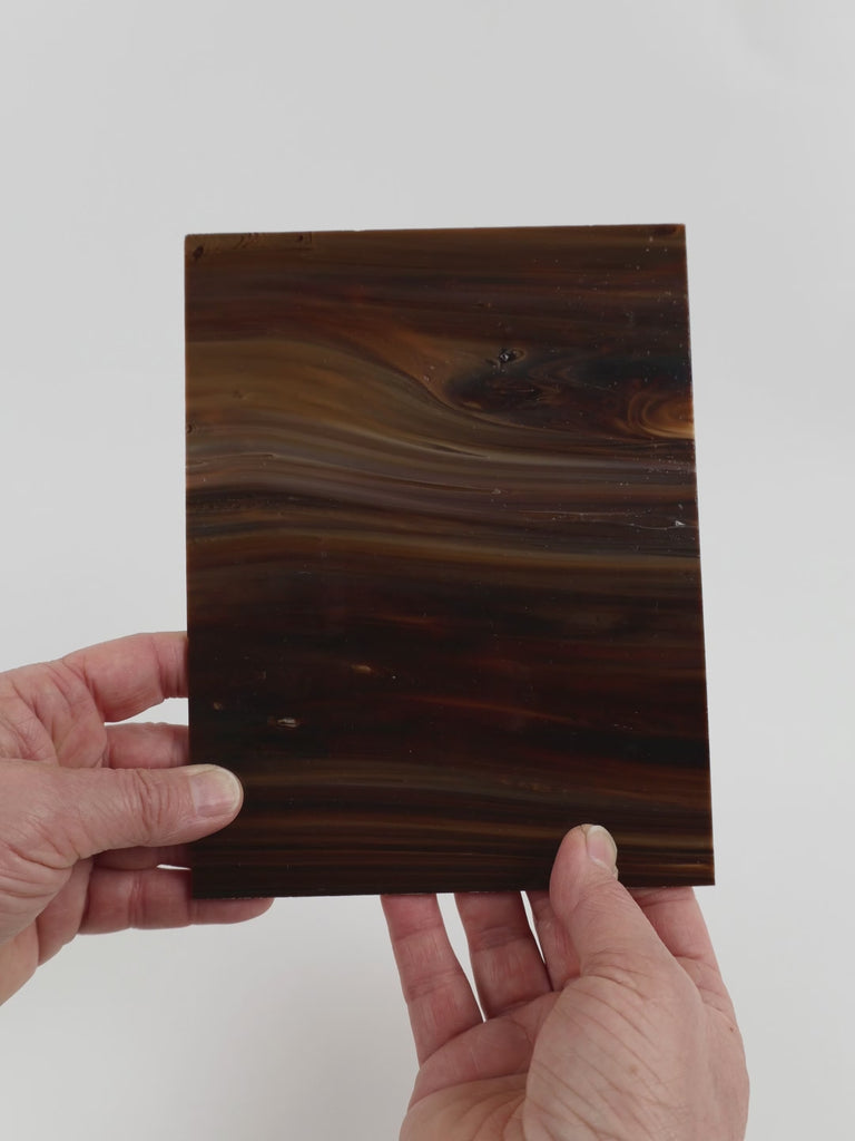 Video of the Nutmeg Streaky glass plate in opaque brown, 15x19cm, held up and tilted to show its pattern and transparency