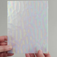 Video of the white pearlescent glass plate in white translucent iridescent, 15x19cm, held up and tilted to show its pattern and transparency
