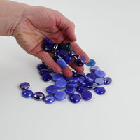 Video of blue mix glass nuggets in cobalt, violet-blue and light blue shades with an iridescent sheen, 16–20 mm, picked up from a pile by hand and dropped back to show their size, round shape and shine