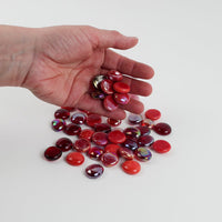 Video of red mix glass nuggets in bright red, cherry and burgundy shades with an iridescent sheen, 16–20 mm, picked up from a pile by hand and dropped back to show their size, round shape and shine